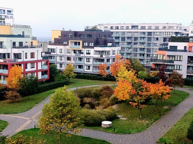 Foto 3 Vnitroblok obytného komplexu s podzimní vegetací. Moderní rezidenční zástavba s přehledným vnitroblokem a udržovanou zelení. Jasně definované pěší trasy a otevřený prostor posilují přirozený dohled a pocit bezpečí.